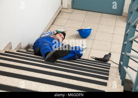 Unconscious Handyman Lying On Staircase With Helmet And Drill On Floor Stock Photo