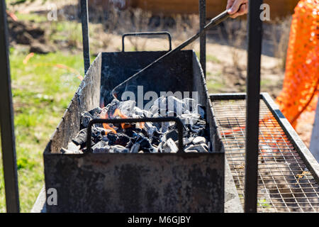 A hand stokes burning coal in a grill, reading for a barbecue on a sunny day Stock Photo