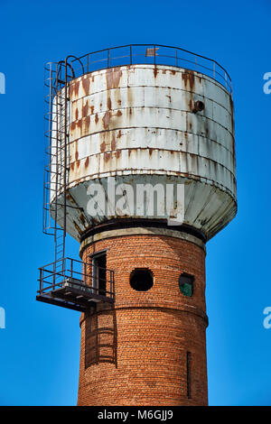 High water-pressure tower made of brick and metal with round windows against the blue sky Stock Photo