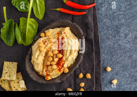 Homemade traditional hummus in a clay dish with spinach and crackers, dark background, top view. Stock Photo
