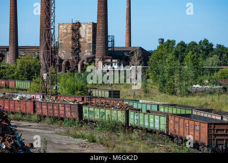 Abandoned industrial complex, with tall, weathered smokestacks towering over the dilapidated buildings against a clear blue sky Stock Photo