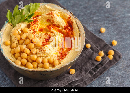 Homemade traditional hummus in a clay dish, dark background, top view. Stock Photo