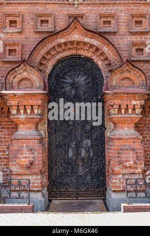 Richly detailed brick wall frames a majestic metal door with intricate wrought ironwork of old chapel Stock Photo