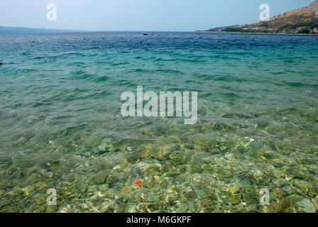 Tranquil coastal scene with clear turquoise waters in the foreground and rocky hills in the background Stock Photo