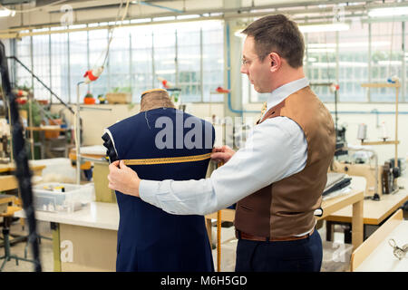 Tailor measuring jacket on mannequin in his workshop Stock Photo