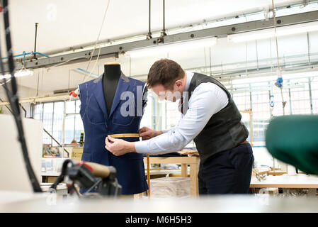 Tailor measuring an incomplete jacket on a mannequin with a measuring tape as he works in his workshop Stock Photo