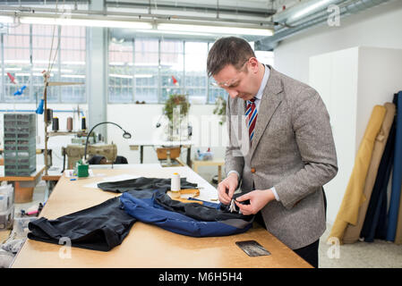 Tailor hand sewing the lining in a blue jacket as he stands at a work table in a spacious bright workshop Stock Photo