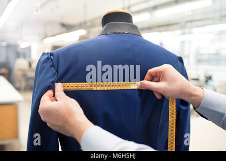 Tailor using measuring tape while doing jacket measurement in workshop Stock Photo
