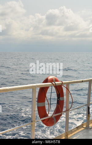 Orange safety buoy hanging on the reiling of a boat, sea in the background. Stock Photo