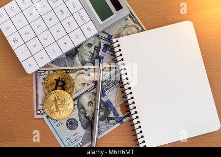 Two golden bitcoins, journal, pen, and calculator on us dollars Stock Photo