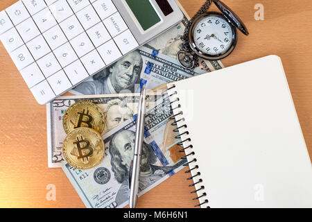 Two golden bitcoins, journal, pen, calculator, and pocket watch on us dollars Stock Photo