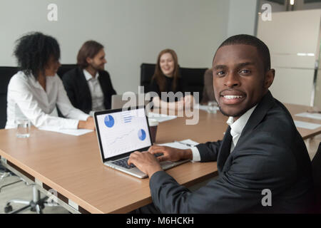 Smiling african-american businessman using laptop looking at cam Stock Photo