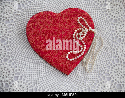 Vintage red fabric Saint Valentine candy box heart against a white doily and pearls, USa, lace Victorian abstract, unconventional Victorian Valentines Stock Photo