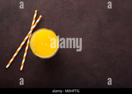 A glass of freshly squeezed orange juice and straws for juice on a dark brown background. Top view with copy space. Stock Photo
