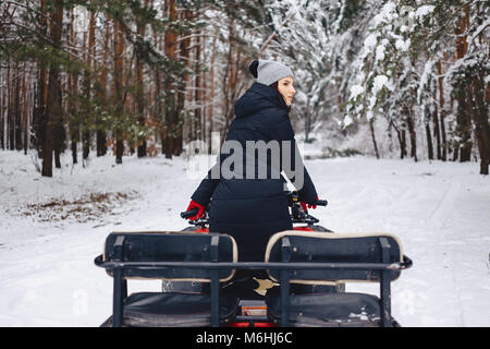 young girl on a motorcycle rides in snow-covered pine forest winters against the background of scenic landscapes Stock Photo
