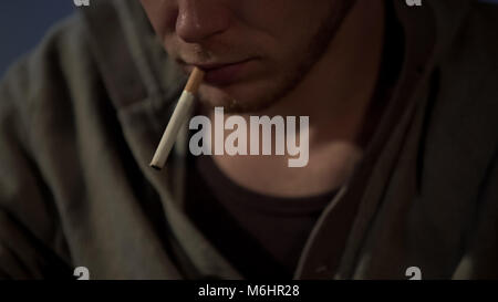 Young man smokes cigarette, depressed and abandoned, health risks, close up Stock Photo