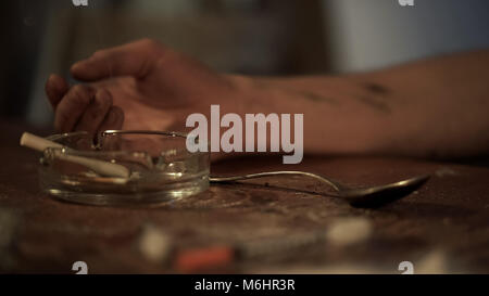 Hand of man suffering drug addiction lying on shabby table at cheap motel room Stock Photo