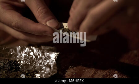Male hands making joint, rolling marijuana into cigarette, drug legalization Stock Photo