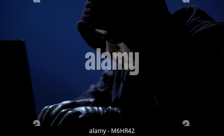 Strange man in black clothes, sunglasses and gloves stealing data from laptop Stock Photo