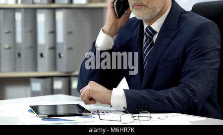 Male company director dialing, talking cell phone, tablet and glasses on table Stock Photo