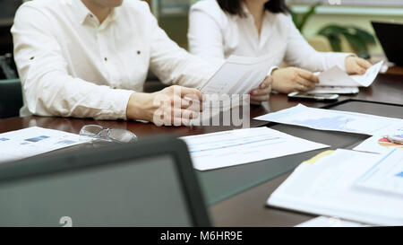 Managers sitting at table in meeting, looking at documents with data bar charts Stock Photo