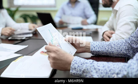 Managers sitting at table in meeting, looking at documents with data bar charts Stock Photo