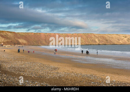 Yorkshire beach winter, view of people walking on the beach in Filey Bay with the cliffs known as Filey Brigg in the background,Yorkshire, England, UK Stock Photo