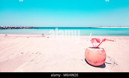 Retro toned wide angle picture of a coconut with two straws and colorful umbrella on a beach, summer holiday concept, selective focus. Stock Photo