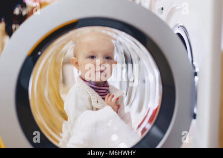 The baby looks through the window of the washing machine and laughs Stock Photo