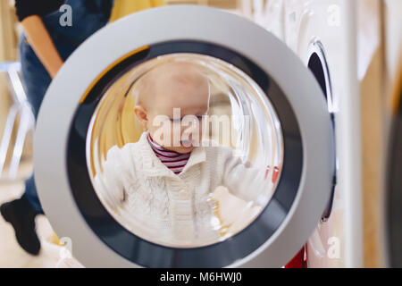 The baby looks through the window of the washing machine and laughs Stock Photo