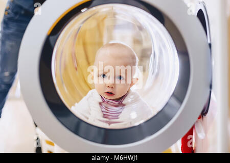 The baby looks through the window of the washing machine and laughs Stock Photo