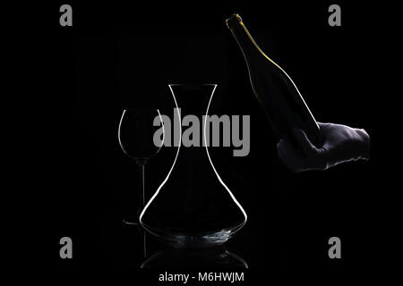 Hand in white glove holds bottle of red wine at bottom and decanter Stock Photo