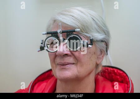 Zrenjanin, SERBIA, February 2018: Elderly woman wearing phoropter or trial frame and looking at mirrored eye test chart during sight test at optometri Stock Photo