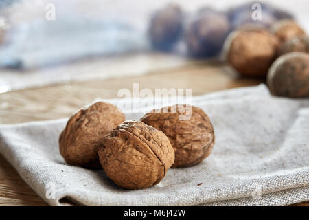 A stack of hard shells of walnuts piled together on light grey fabric cotton napkin and isolated on rustic wooden background, copy space, shallow dept Stock Photo