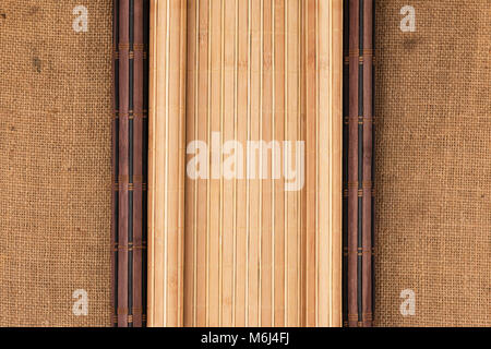 Dark and light bamboo mat in the form of a scroll lie on the sacking. View from above. Stock Photo