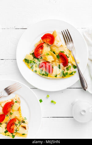 Omelet. Eggs fried. Scrambled eggs with green onion and fresh tomato. Omlette on white plate. Breakfast. Top view. White wooden background Stock Photo