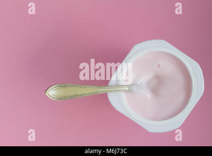 Healthy strawberry fruit flavored yoghurt with natural coloring in plastic cup isolated on pink background with space for text and small silver spoon  Stock Photo
