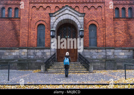 A girl standing toward a red brick building in autumn, in the center of Malmo, Sweden. Stock Photo