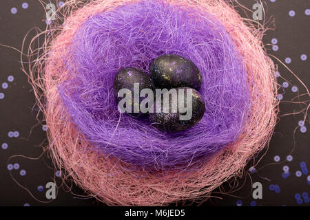 Background image of galaxy-like painted Easter eggs lying in nest of colored straw on table, above view Stock Photo