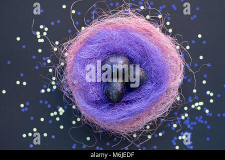 Background image of galaxy-like painted Easter eggs lying in nest of colored straw on table in neon light, above view Stock Photo