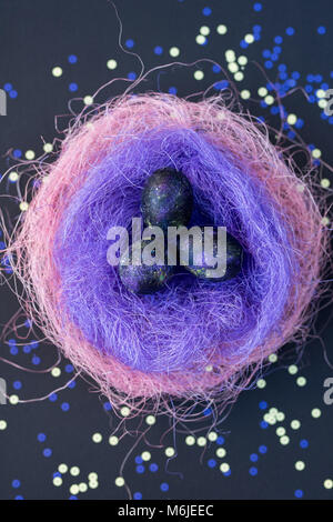 Background image of glittering spray-painted Easter eggs lying in nest of colored straw on table in neon light, above view Stock Photo
