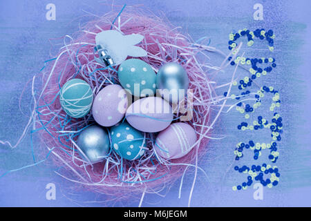 Background image of cute pastel-colored eggs lying in pink nest with word EASTER above in glitter, copy space Stock Photo