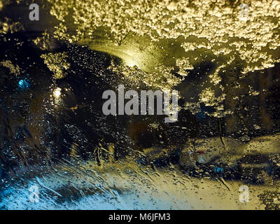 Raindrops and melting snow on the car window at night illuminated by street lights during heavy rain background Stock Photo