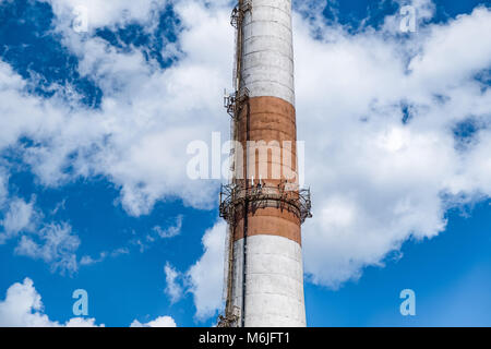 Brick chimney of a factory boiler room. Brick chimney with red and white stripes on a cloudy sky background Stock Photo