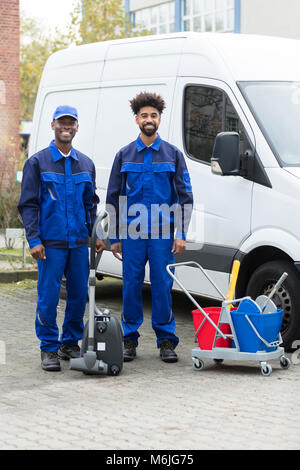 Portrait Of Two Happy Male Janitor Standing With Cleaning Equipment Against Truck Stock Photo