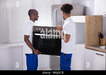 Two Male Workers In Uniform Fixing The Oven In The Kitchen At Home Stock Photo