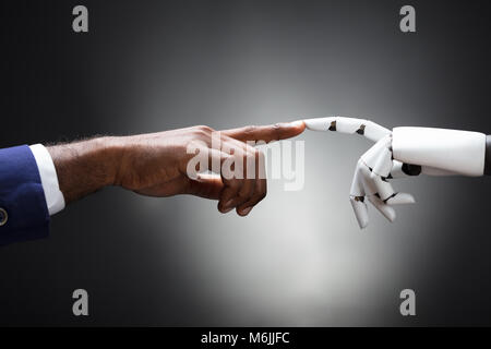 Fingers Of Robot And Man Touching Against Gray Background Stock Photo