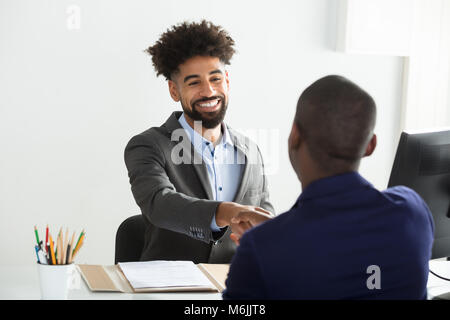Smiling Young Businessman Shaking Hand With Male Candidate In Office Stock Photo