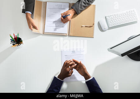 Elevated View Of Businessperson And Candidates Hand With Resume On White Desk Stock Photo
