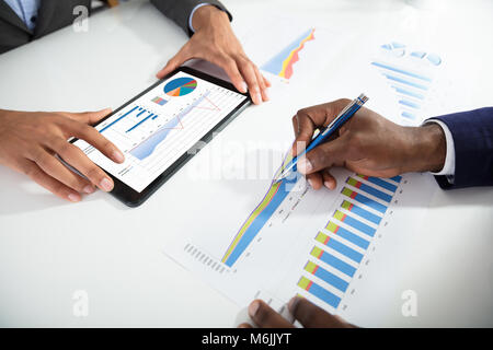 Two Businesspeople Using Digital Tablet While Analyzing Graph In Office Stock Photo